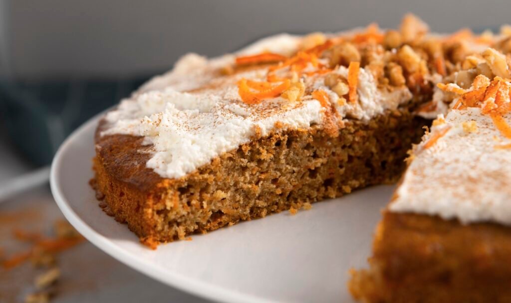 Bolo de cenoura com cobertura de cream cheese, decorado com raspas de cenoura e nozes.