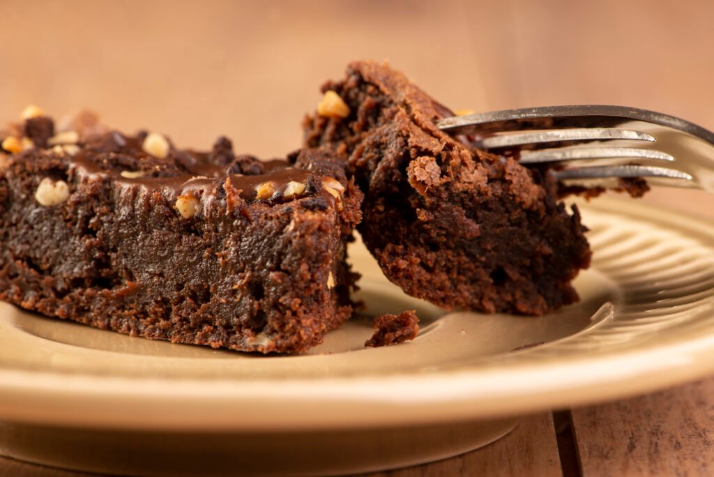 Fatia de bolo de chocolate fit com cobertura cremosa e pedaços de nozes.