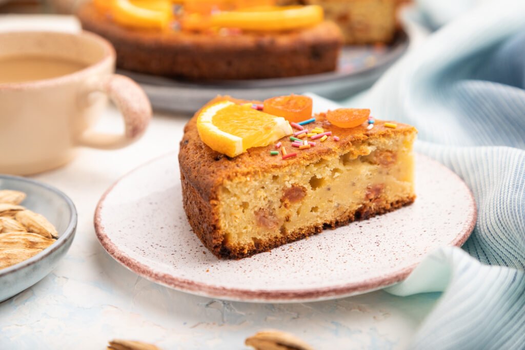 Fatia de bolo de laranja com amêndoas decorada com laranja e confeitos coloridos.