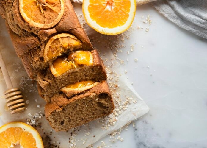 Bolo de laranja fit com fatias de laranja decorativas, servido em uma superfície de mármore.