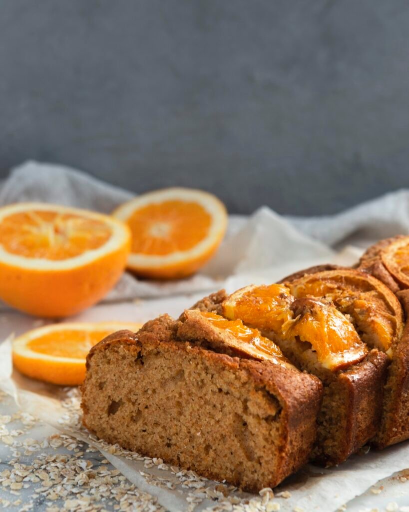 Bolo de laranja fit fatiado, com pedaços de laranja decorativos ao fundo.