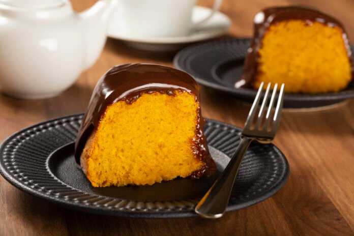 Fatia de bolo de cenoura com cobertura de chocolate em prato preto