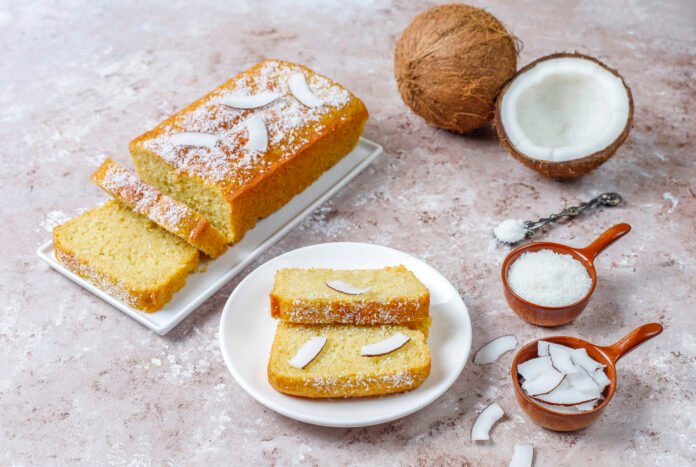 Fatia de bolo de abacaxi com coco integral decorado com coco ralado e lascas de coco.