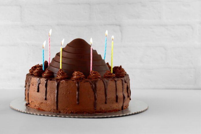 Bolo de aniversário com cobertura de chocolate e velas coloridas.