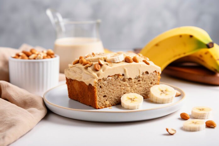 Bolo de banana vegano com aveia decorado com cobertura de amendoim e fatias de banana.