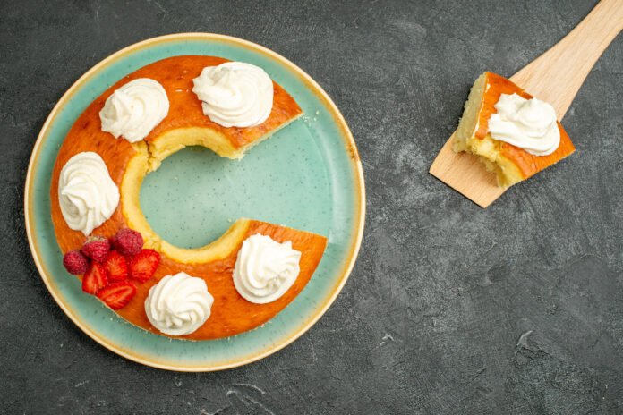 Bolo de baunilha fofinho decorado com chantilly e frutas vermelhas em um prato verde.