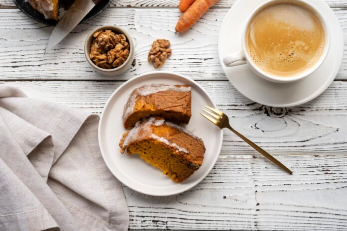 Fatias de bolo de café com leite ao lado de uma xícara de café e nozes sobre uma mesa branca.