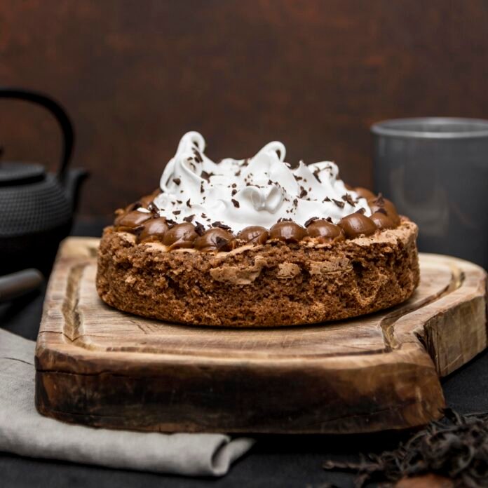 Bolo de chocolate com creme de leite decorado com chantilly e raspas de chocolate em uma base rústica de madeira.