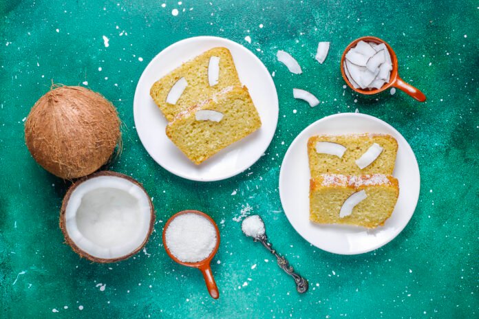 Fatias de bolo de coco vegano acompanhadas de coco ralado e lascas de coco fresco sobre fundo verde.