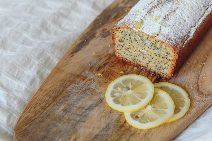 Bolo de limão vegano com sementes de chia decorado com fatias de limão sobre uma tábua de madeira.