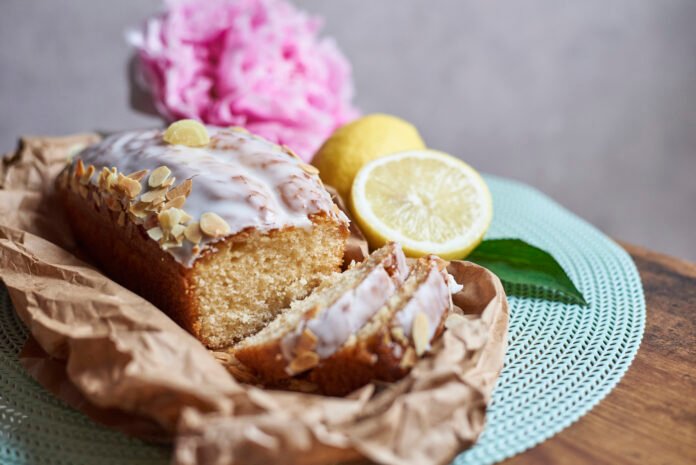 Bolo de limão com aveia decorado com amêndoas e cobertura de limão, servido em papel rústico.