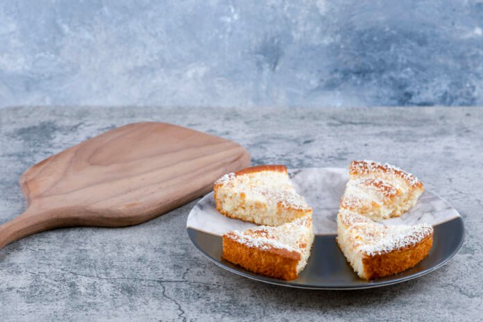 Fatias de bolo de mandioca fofinho e úmido servidas em um prato, decoradas com coco ralado.