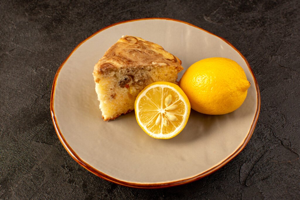 Fatia de bolo de limão com aveia ao lado de um limão inteiro e meio limão em um prato.