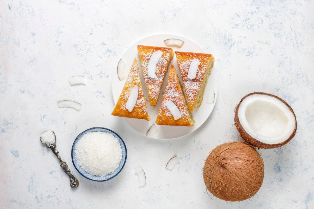 Fatia de bolo de abacaxi com coco integral decorada com coco ralado e pedaços de coco fresco.