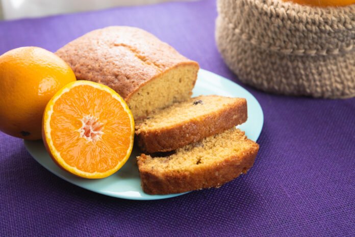 Bolo de laranja diet fatiado em prato azul com laranja ao lado.