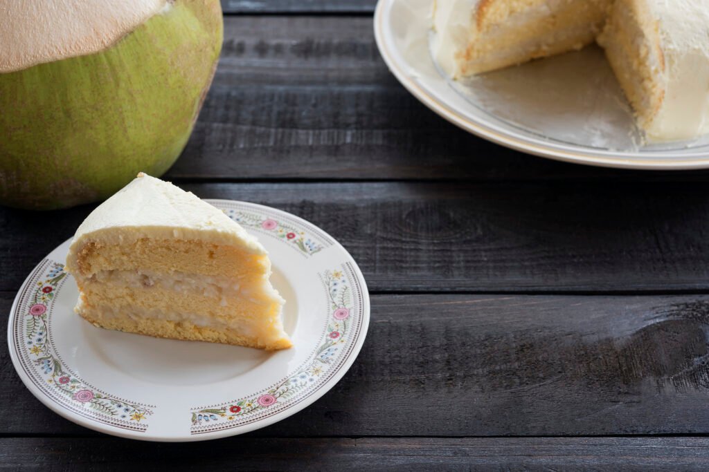 Fatia de bolo de abacaxi com coco integral em prato decorado, ao lado de um coco fresco.