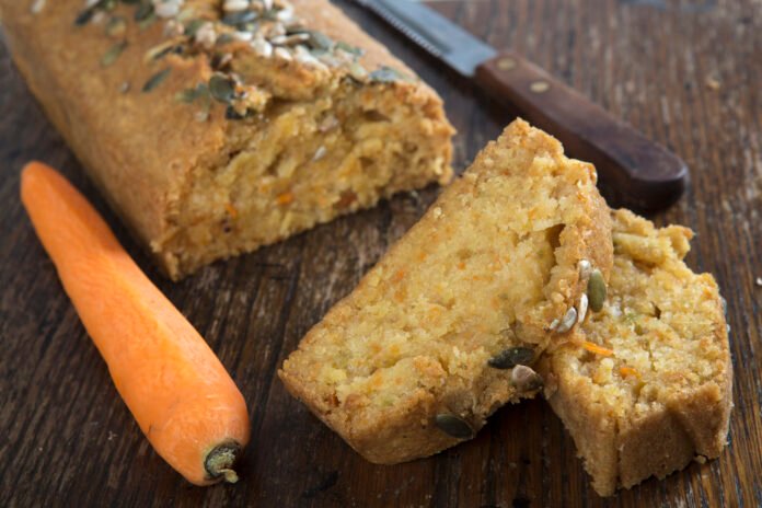 Bolo Integral de Cenoura com Sementes de Chia sobre uma mesa de madeira, com fatias cortadas e cenoura fresca ao lado.