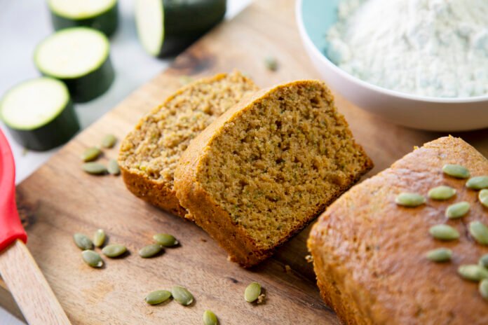 Fatias de bolo integral de fubá com erva-doce decoradas com sementes de abóbora sobre uma tábua de madeira.