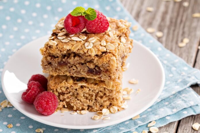 Fatias de bolo de aveia com castanhas e frutas secas, decoradas com framboesas frescas.