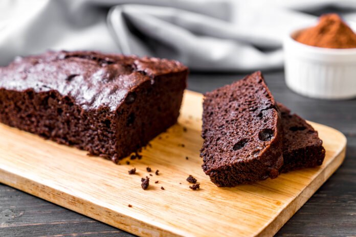 Bolo de batata doce com cacau fit servido em uma tábua de madeira, com fatias destacadas e fundo de tecido cinza.