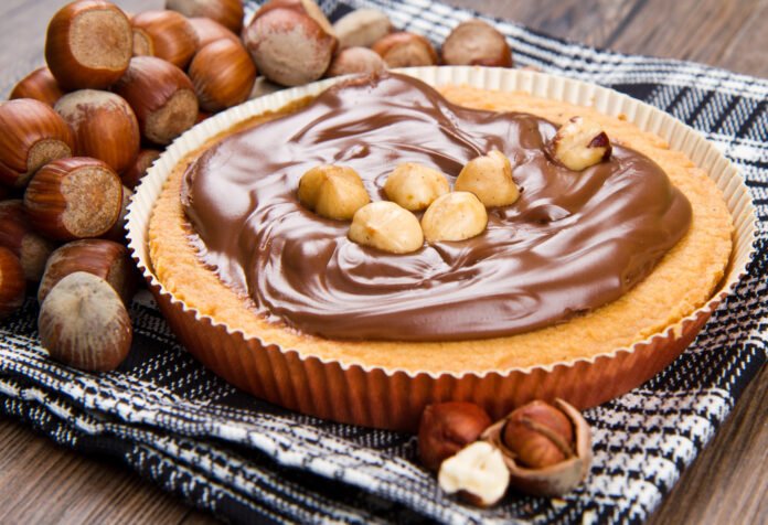 Bolo de cenoura fofinho com cobertura de creme de avelã e avelãs inteiras como decoração.