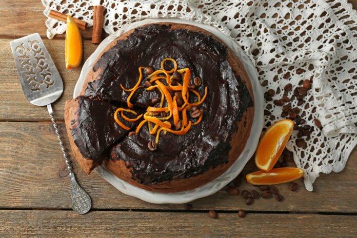 Bolo de chocolate com laranja decorado com raspas de laranja e cobertura brilhante.