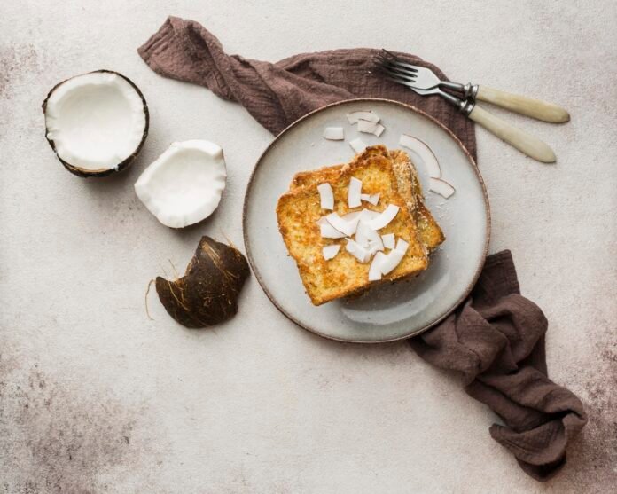 Bolo de coco com leite de amêndoas sem açúcar servido em um prato com pedaços de coco fresco ao lado.