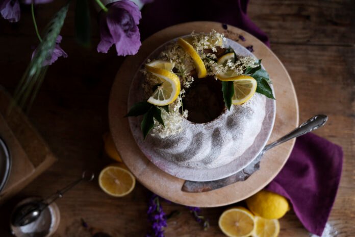 Bolo decorado com limão e flores de lavanda em uma mesa rústica, perfeito para uma sobremesa refinada.