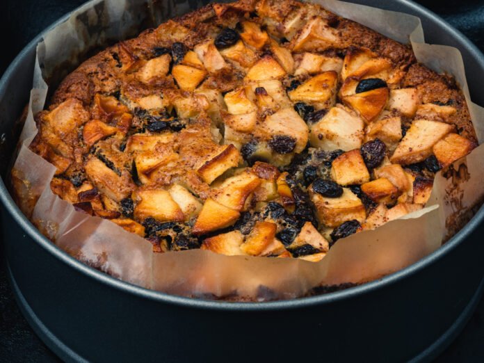 Bolo de maçã e passas caseiro com pedaços de maçã caramelizada e passas em uma forma redonda.