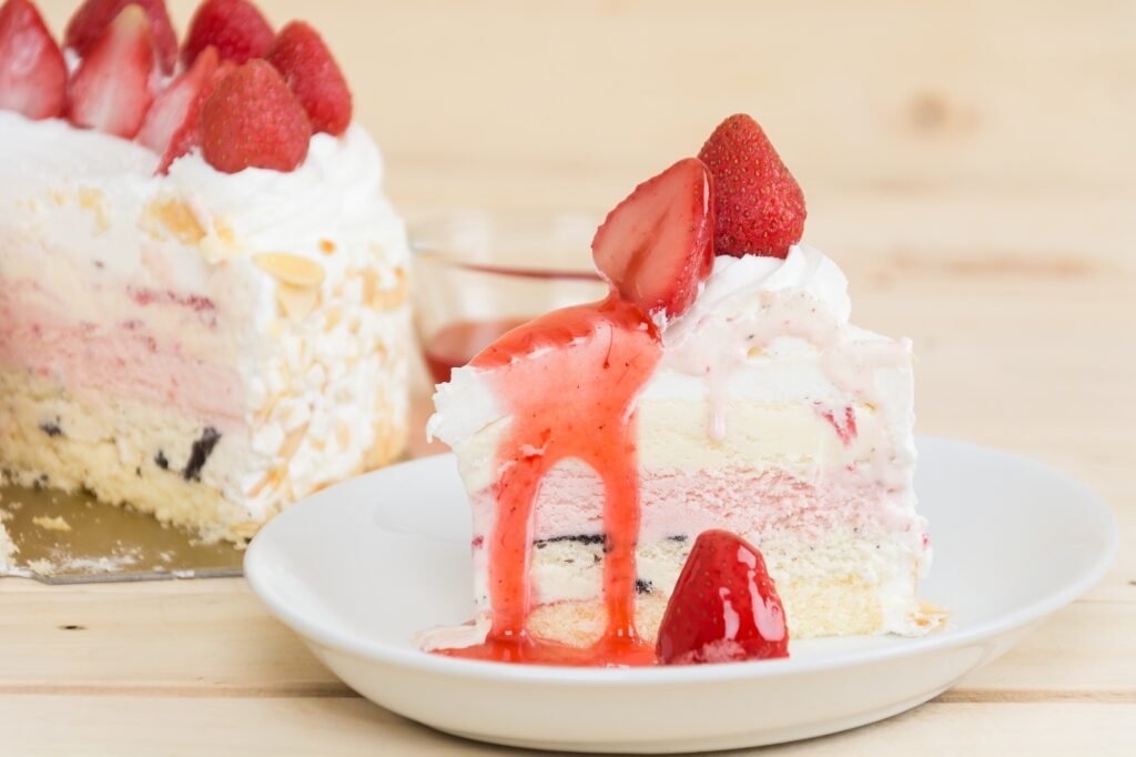 Fatia de bolo gelado de leite ninho com cobertura de morango e pedaços de fruta fresca.