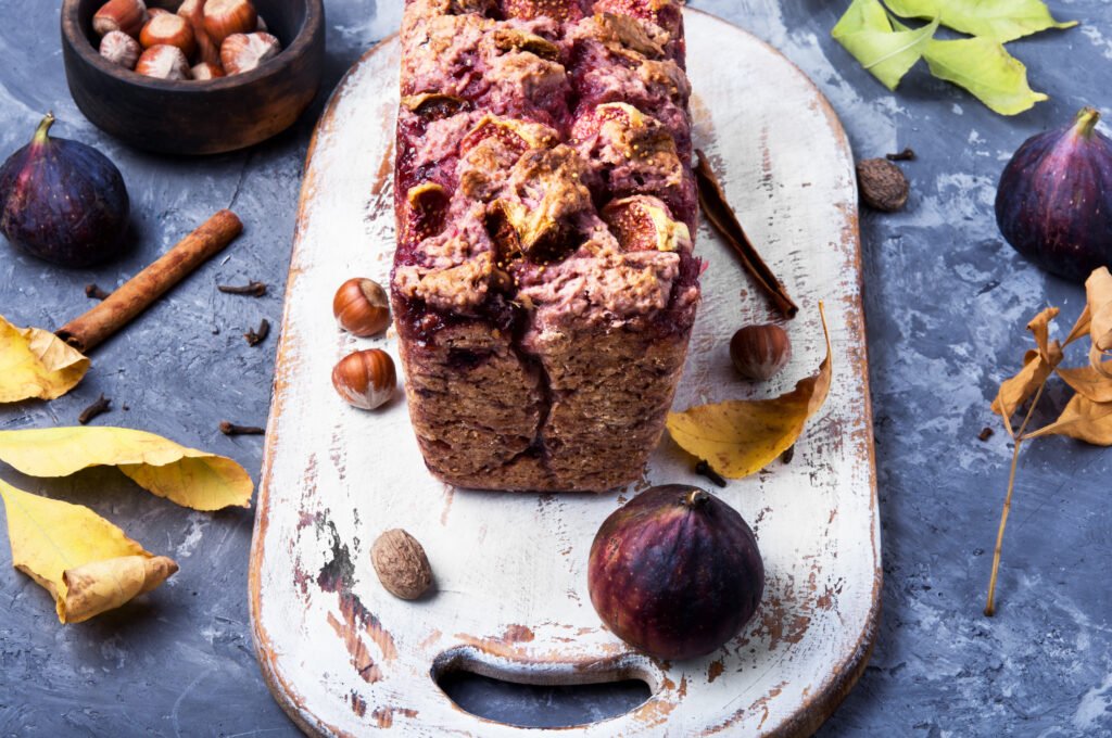 Bolo de ameixa com especiarias sem açúcar decorado com frutas e especiarias em uma tábua rústica.