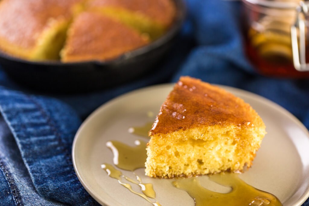 Fatia de bolo de milho com coco e mel em um prato com calda de mel.