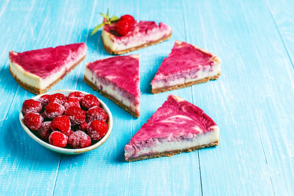 Fatias de bolo gelado de iogurte natural com frutas vermelhas sobre uma mesa azul.