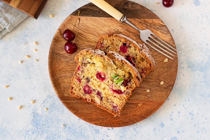 Fatias de bolo de aveia com frutas vermelhas vegano servidas em um prato rústico de madeira, decorado com cerejas frescas e açúcar polvilhado.