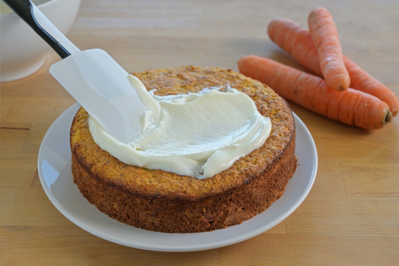 Preparação de um bolo de cenoura integral com iogurte sendo coberto com creme.