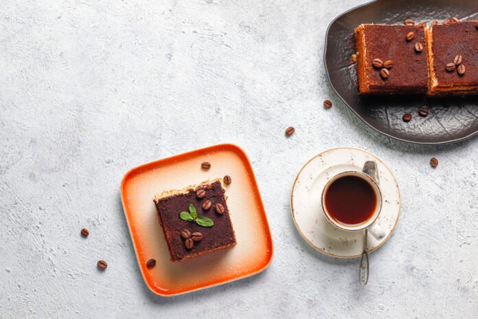 Bolo de chocolate com café servido em um prato laranja com uma xícara de café ao lado.