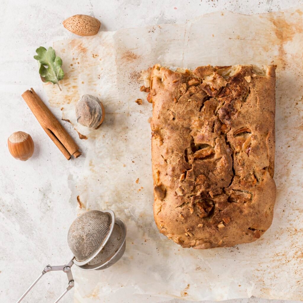 Bolo de canela com nozes inteiro em papel manteiga, decorado com especiarias e nozes.