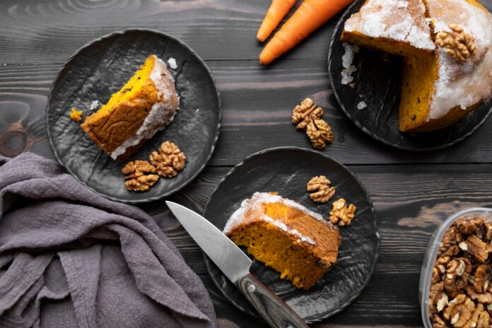 Fatias de bolo de cenoura com casca decoradas com nozes em um prato escuro.