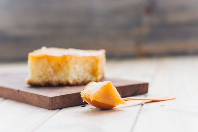 Fatia de bolo de fubá com queijo Minas sobre uma tábua de madeira, acompanhada de uma colher com pedaço do bolo.