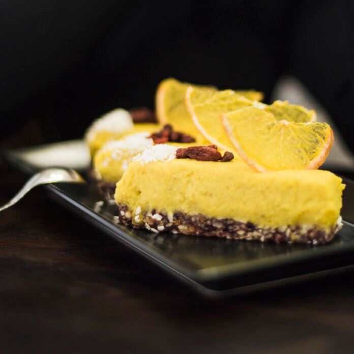 Fatia de bolo de maracujá com raspas de limão decorada com rodelas de laranja e frutas secas.