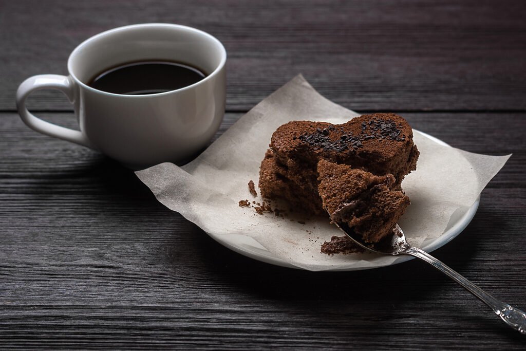 Fatia de bolo de chocolate com café em formato de coração, acompanhada de uma xícara de café preto.