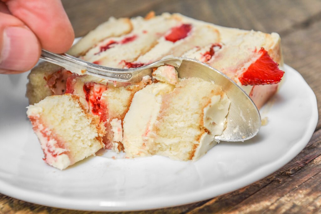 Fatia de bolo de iogurte com morango em um prato branco, destacando a textura macia e os pedaços de morango.