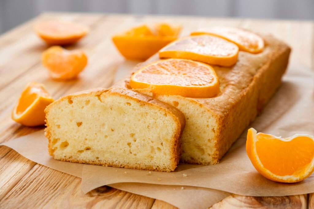 Fatias de bolo de laranja com gengibre decoradas com rodelas de laranja fresca, sobre uma base de papel manteiga.